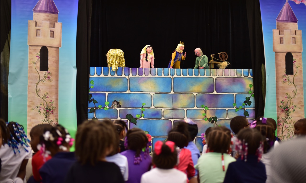 An audience of children watching a puppet show on a stage.