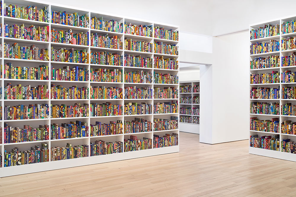 Yinka Shonibare's past work shown in a photograph of many books on bookshelves spanning multiple rooms.
