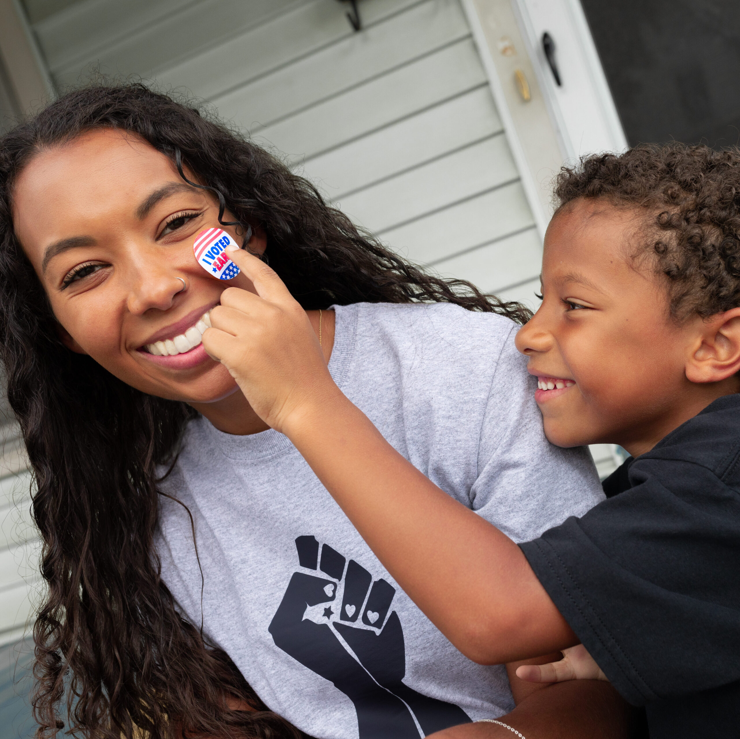 African American son placing I Voted Early Sticker on smiling black mother's face
