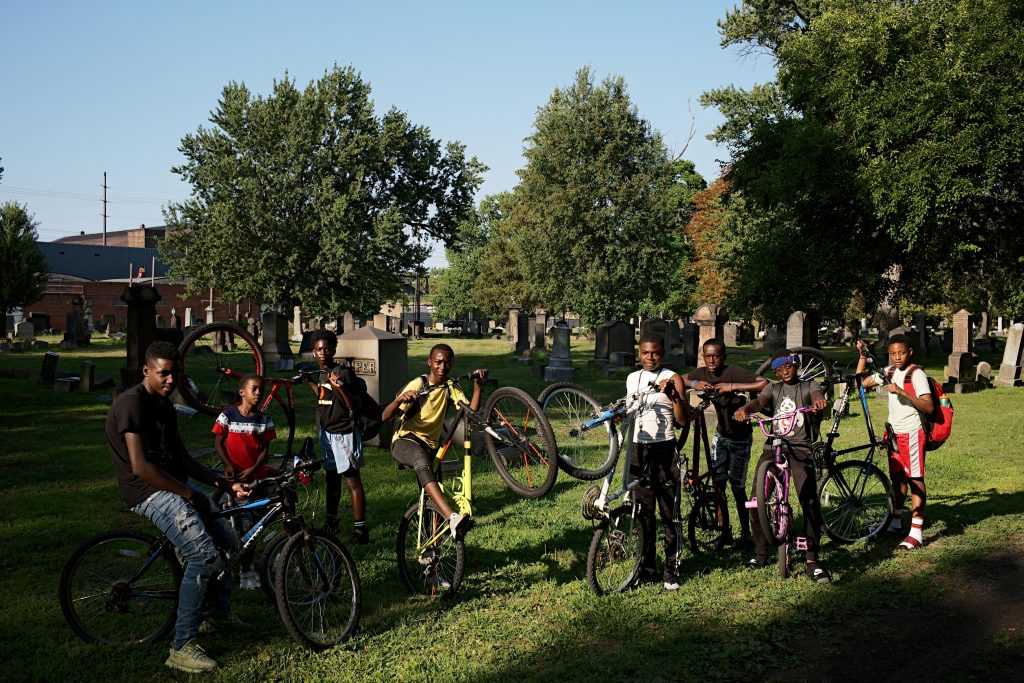 large group of boy with bikes stand in a cemetery facing camera