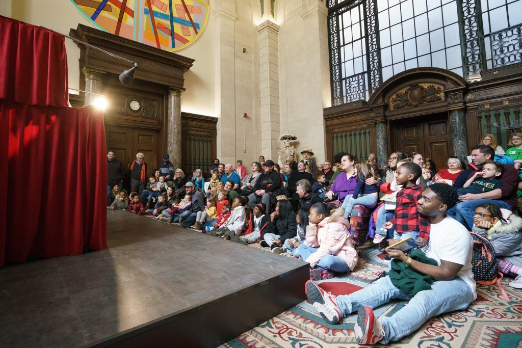 Room of children and parents sitting on the floor in front of a puppet stage.